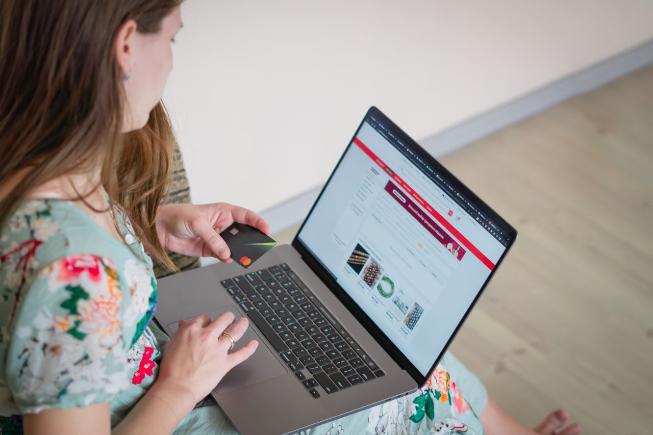 project-03-a Žena u cvjetnoj haljini kupuje online uz prijenosno računalo i kreditnu karticu u zatvorenom prostoru.